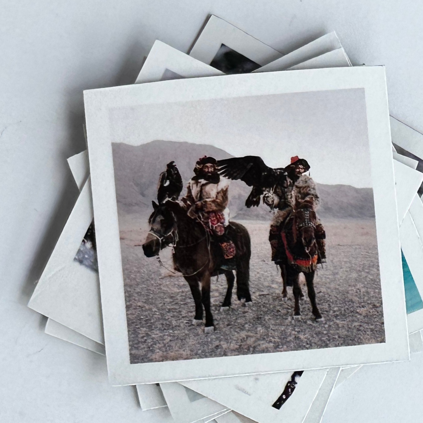 Stack of magnetic photo prints featuring people on horseback with eagles against a mountainous background.